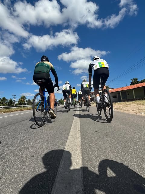 Pelotão do Magrela na estrada, visto de trás, céu azul